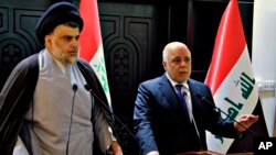 In this photo provided by the Iraqi government, Iraqi Prime Minister Haider al-Abadi, right, and Shiite cleric Muqtada al-Sadr hold a press conference in the heavily fortified Green Zone in Baghdad, Iraq, May 20, 2018. 