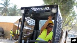 Roselette Dupervil, a heavy machinery operator, talks to a colleague from her seat inside an excavator as she clears rubble. She is one of 30 women who went through training at the Haytrac Center, a training facility funded by USAID.