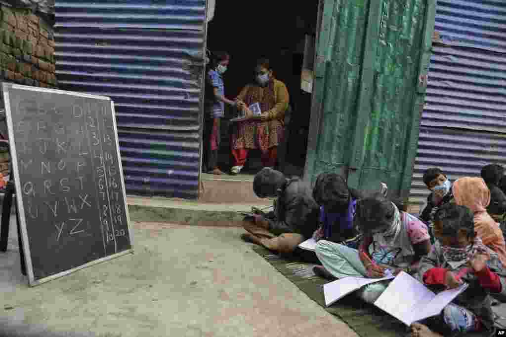 A teacher wearing face mask checks the note books of children at the Sangharsh Vidya Kendra school at a slum area on the outskirts of Jammu, India.