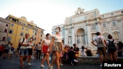 Transeúntes y turistas con máscaras junto a la Fuente de Trevi, una de las principales atracciones de Roma.