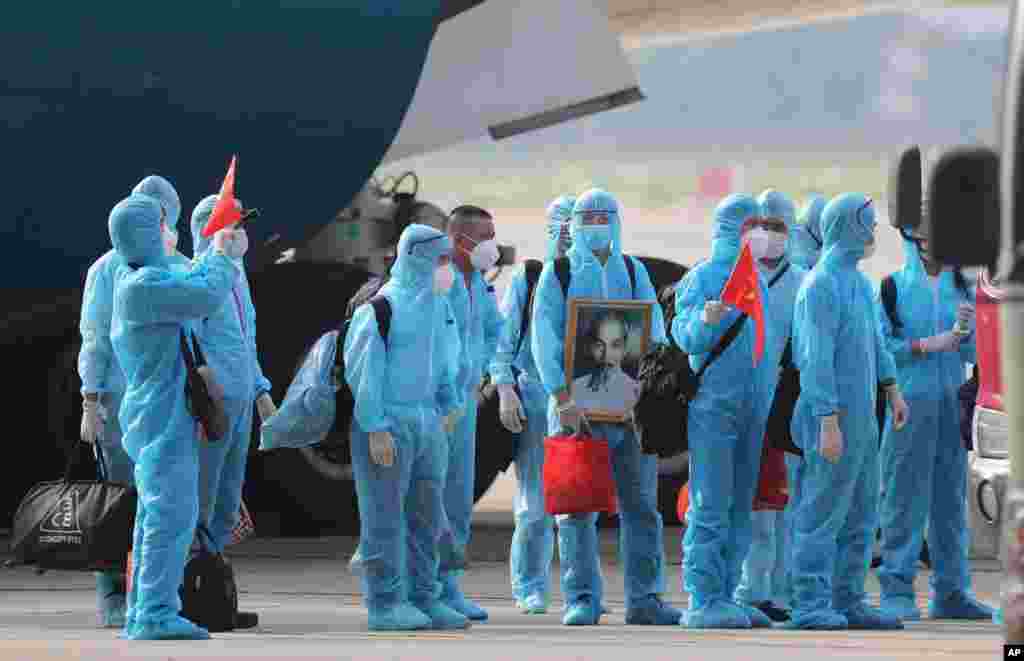 Vietnamese COVID-19 patients, who were working in Equatorial Guinea, hold Vietnamese flags and carry a portrait of deceased national leader Ho Chi Minh, as they arrive at the Noi Bai Airport in Hanoi.