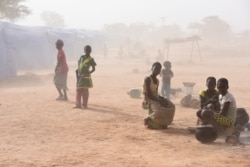 Displaced people, who fled from attacks of armed militants in Roffenega, are engulfed in dust as they sit at the camp built by the German NGO HELP in Pissila, Burkina Faso, Jan. 24, 2020.