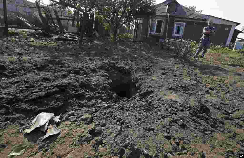 A local man stands next to a shell crater with his destroyed house in the background, in Donetsk, eastern Ukraine,&nbsp; Aug. 14, 2014.