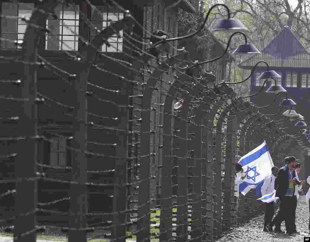 یک گروه از بازدید کنندگان با پرچم اسرائیل در اردوگاه &laquo;آشویتس&raquo; در دوران آلمان نازی که اکنون در لهستان قرار دارد. هولوکاست یادآور نسل کشی یهودیان است که نازی&zwnj;ها دست کم شش میلیون یهودی را کشتند.