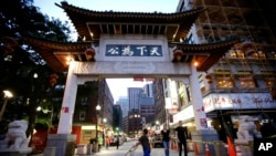 Faces of Chinatown: In this Monday, Aug. 29, 2016 photo a child pushes a stroller under a gate to Boston's Chinatown neighborhood. Artist Wen-ti Tsen, who plans to install life-sized portraits on the street around the neighborhood beginning Sept. 10, says they're meant to underscore how the city's building boom is displacing longtime residents and businesses in the historic downtown enclave. 