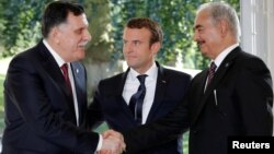 FILE - French President Emmanuel Macron stands between Libyan Prime Minister Fayez al-Sarraj (L), and General Khalifa Haftar (R), commander in the Libyan National Army (LNA), who shake hands after talks over a political deal to help end Libya’s crisis in La Celle-Saint-Cloud near Paris, France, July 25, 2017. 