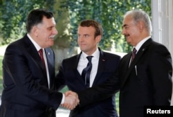 FILE - French President Emmanuel Macron stands between Libyan Prime Minister Fayez al-Serraj, left, and General Khalifa Haftar, commander in the Libyan National Army, who shake hands after talks over a political deal to help end Libya’s crisis in La Celle-Saint-Cloud near Paris, France, July 25, 2017.