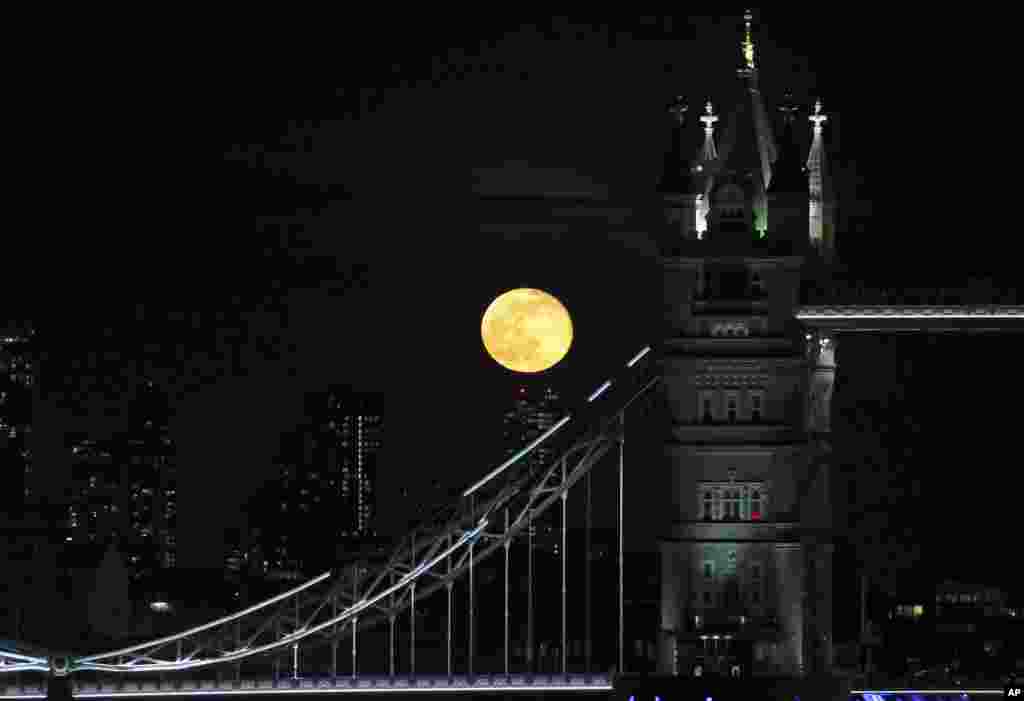 A full moon rises over the high buildings behind Tower Bridge in central London, March 29, 2021.