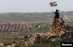 A protester waves a Palestinian flag in front of the Jewish settlement of Ofra during clashes near the West Bank village of Deir Jarir near Ramalla,h Apr. 26, 2013.