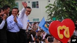 Opposition Cambodia National Rescue Party (CNRP) leader Sam Rainsy, right, accompanied by his party's Vice President Kem Sokha, second from right, waves to his party supporters during a public forum of the July 28 election result, in Phnom Penh, Cambodia, Monday, Aug. 26, 2013. Rainsy told thousands of supporters that his party will stage massive protests unless an independent committee begins investigating alleged irregularities in last month's election. (AP Photo/Heng Sinith)