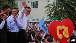 Opposition Cambodia National Rescue Party (CNRP) leader Sam Rainsy, right, accompanied by his party's Vice President Kem Sokha, second from right, waves to his party supporters during a public forum of the July 28 election result, in Phnom Penh, Cambodia, Monday, Aug. 26, 2013. Rainsy told thousands of supporters that his party will stage massive protests unless an independent committee begins investigating alleged irregularities in last month's election. (AP Photo/Heng Sinith)