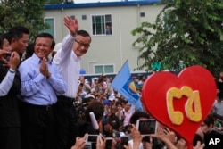Opposition Cambodia National Rescue Party (CNRP) leader Sam Rainsy, right, accompanied by his party's Vice President Kem Sokha, second from right, waves to his party supporters during a public forum of the July 28 election result, in Phnom Penh, Cambodia, Monday, Aug. 26, 2013.