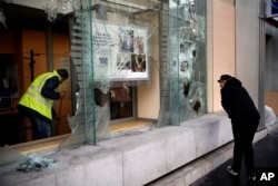 FILE - A worker clears debris in a bank as a man watches through smashed windows, in Paris, Dec. 9, 2018.