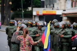 A woman holding a Venezuelan national flag heckles Bolivarian National Guardsmen blocking the passage of opposition members during a protest march against President Nicolas Maduro in Caracas, Venezuela, Jan. 23, 2019.