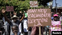 FILE - Supporters of the PHTK political party hold signs during a demonstration to demand the organization of a postponed presidential runoff election in Port-au-Prince, Haiti, April 14, 2016. 
