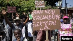 FILE - Supporters of PHTK political party hold signs during a demonstration to demand the organization of a postponed presidential runoff election in Port-au-Prince, Haiti, April 14, 2016. 