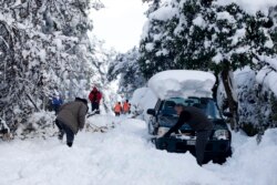 Warga di pinggiran kota Dionysos, Athena utara, membersihkan jalanan yang tertutup salju tebal, Rabu, 17 Februari 2021.