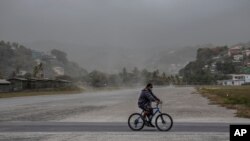 A man rides his bicycle past fields covered with volcanic ash a day after the La Soufriere volcano erupted, in Kingstown, on the eastern Caribbean island of St. Vincent, April 10, 2021.