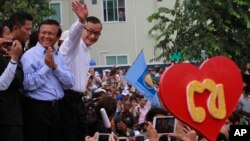 Opposition Cambodia National Rescue Party (CNRP) leader Sam Rainsy, right, accompanied by his party's Vice President Kem Sokha, second from right, waves to his party supporters during a public forum of the July 28 election result, in Phnom Penh, Cambodia, Monday, Aug. 26, 2013. Rainsy told thousands of supporters that his party will stage massive protests unless an independent committee begins investigating alleged irregularities in last month's election. (AP Photo/Heng Sinith)