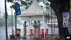 Policemen enforcing a lockdown to curb the spread of coronavirus stand beneath a rain shelter in Kochi, Kerala state, India, Sunday, May 16, 2021. A severe cyclone is roaring in the Arabian Sea off southwestern India with winds of up to 140…