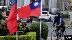 FILE - This photo taken on Dec. 22, 2023, shows a cyclist next to two Taiwanese national flags in Taipei.