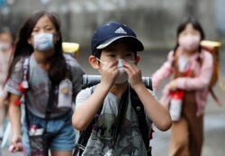 FILE - Children, wearing protective masks amid the coronavirus pandemic, arrive at their elementary school, which practices various methods of social distancing, in Funabashi, east of Tokyo, Japan, July 16, 2020.