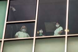 FILE - Nurses look out from a window of the San Luca Hospital in Milan, Italy, April 30, 2020.
