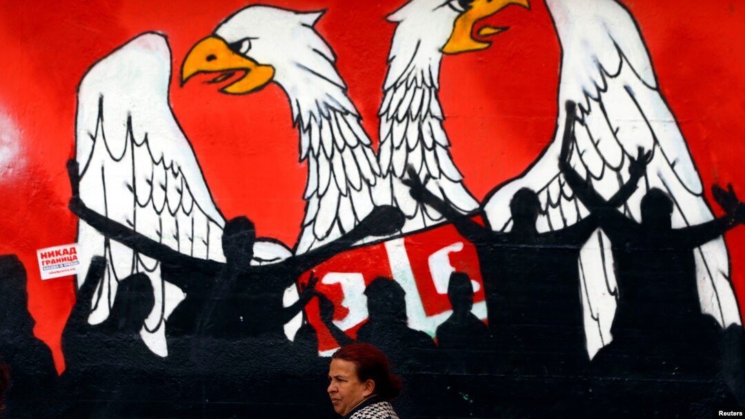 A woman walks past a graffiti depicting part of the Serbian coat of arms in the northern Serb dominated, part of the ethnically divided town of Mitrovica, Kosovo, April 3, 2013.