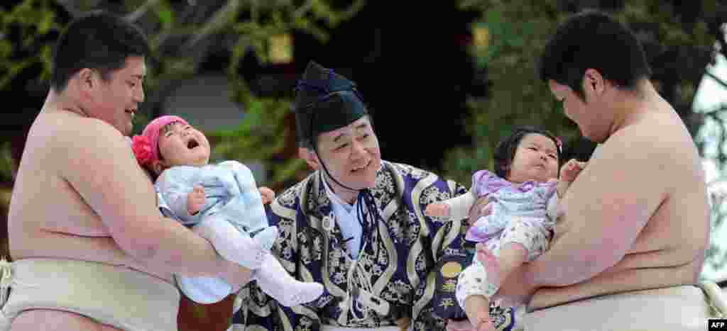 Dua mahasiswa pegulat sumo membawa bayi yang menangis di samping wasit (tengah) dalam acara Kompetisi &#39;Bayi Menangis&#39; di kuil Sensoji di Tokyo, Jepang.