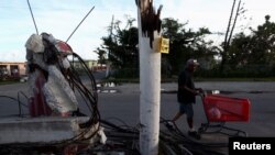 ARCHIVO - Un hombre empuja un carrito de supermercado detrás de un poste de luz parcialmente colapsado y cables caídos, después que el huracán María azotó la isla en septiembre de 2017. Humacao, Puerto Rico, enero 25 de 2018.