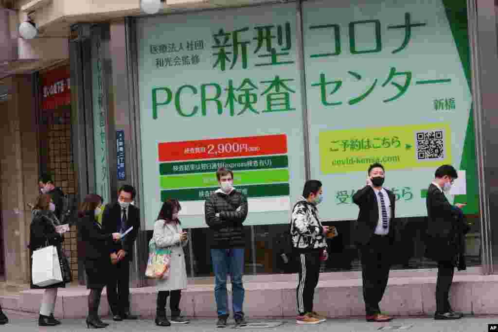 گروهی از مردم، که برای محافظت از خود در برابر شیوع ویروس جدید کرونا ماسک به صورت زده‌اند، برای انجام آزمایش کرونا در خارج از ساختمان پی سی آر تستینگ توکیو در ژاپن صف کشیده‌اند.