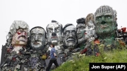 Seorang pengunjung berjalan melewati patung yang dibuat dari limbah elektronik yang menyerupai Gunung Rushmore dan para pemimpin G-7 di sebuah bukit di Hayle, Cornwall, Inggris, Rabu, 9 Juni 2021. (Foto: AP/Jon Super)