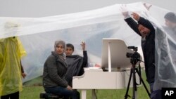 Pembangkang China Ai Weiwei (kanan) menaungi pemain piano Suriah, Nour Alkhzam di tengah hujan deras di Idomeni, Yunani (12/3). (AP/Vadim Ghirda)