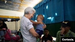 La hermana Rosita sostiene a Alexander Solis y saluda a los refugiados y migrantes venezolanos mientras esperan para recoger los kits de higiene y nutrición donados por el IMDH en la Casa de Acolhida São José, en Pacaraima, Brasil. [Foto: ACNUR]