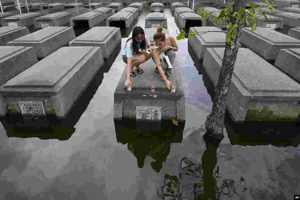 Women place candles on the half-submerged tomb of family members at flood-prone Holy Spirit Memorial Park in Masantol, Pampanga province, Philippines after heavy rains from Tropical Storm Trami, ahead of All Saints Day.