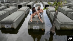 Women place candles on the half-underwater tomb of family members at Holy Spirit Memorial Park in Masantol, Pampanga province, Philippines after heavy rains from Tropical Storm Trami, ahead of All Saints Day.