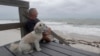 Kent Ejren i njegov pas Blanko posmatraju talase koje donosi tropska oluja Isaias, u blizini Džejsi bič parka, 2. avgusta 2020, u Vero Biču, Florida.