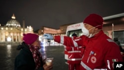 A red cross volunteer checks the temperature of a homeless woman, in front of St. Peter's Square, in Rome, March 25, 2020. 