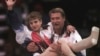 FILE - USA's Kerri Strug is carried by her coach, Bela Karolyi, as she waves to the crowd on her way to receiving her gold medal for the women's team gymnastics competition, at the Summer Olympic Games in Atlanta, July 23, 1996.