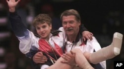 FILE - USA's Kerri Strug is carried by her coach, Bela Karolyi, as she waves to the crowd on her way to receiving her gold medal for the women's team gymnastics competition, at the Summer Olympic Games in Atlanta, July 23, 1996.