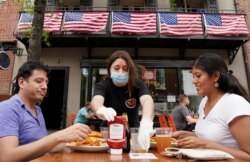 Cuando comienza la Fase Uno de reapertura en el norte de Virginia, una camarera con una máscara facial para protegerse contra la enfermedad por coronavirus (COVID-19) sirve a los comensales en un restaurante en Alexandria, Virginia, EE. UU.