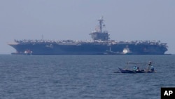 FILE: Fishermen on board a small boat pass by the USS Carl Vinson aircraft carrier at anchor off Manila, Philippines, Feb. 17, 2018.