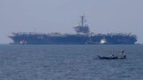 Fishermen on board a small boat pass by the USS Carl Vinson aircraft carrier at anchor off Manila, Philippines, Feb. 17, 2018. 