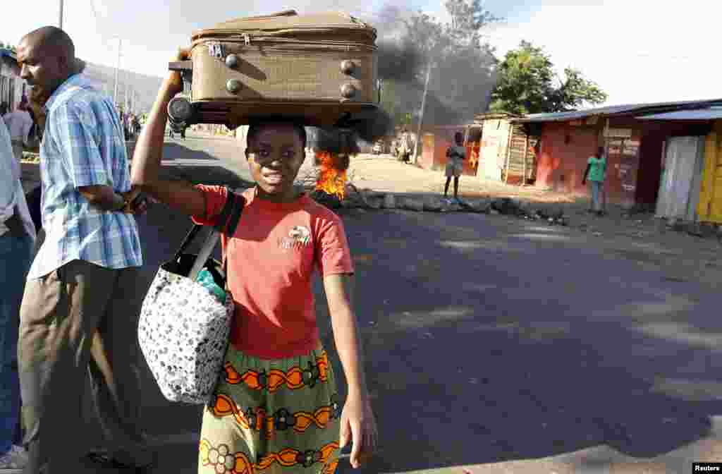 Seorang perempuan membawa koper ketika meninggalkan bentrokan antara polisi anti huru-hara dan demonstran menentang keputusan partai berkuasa CNDD-FDD untuk mengijinkan Presiden Pierre Nkurunziza mencalonkan diri untuk masa jabatan lima tahun ketiga kalinya, di Bujumbura, Burundi.