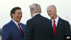 El presidente Donald Trump (de espaldas) conversa con el candidato republicano a gobernador de la Florida Ron DeSantis (izq) y con el gobernador saliente Rick Scott, aspirante a una banca en el Senado nacional, a su llegada a Fort Myers, Florida, el 31 de octubre del 2018.
