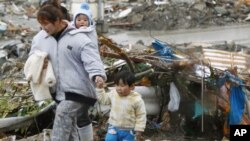 Woman and her children walk past earthquake-damaged homes