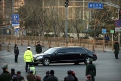 FILE - Security officials stand guard while a Mercedes limousine in a motorcade believed to be carrying North Korean leader Kim Jong Un passes along a street in Beijing, Jan. 9, 2019.