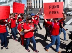 FILE - A teacher carries a placard in support of funding the teacher and other public-sector workers' pension fund during a rally in Denver, April 27, 2018.