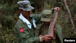Một thành viên nhóm nổi dậy MNDAA đặt khẩu súng máy và băng đạn lên vai một chiến binh trong căn cứ quân sự vùng Kokang 10.3.15