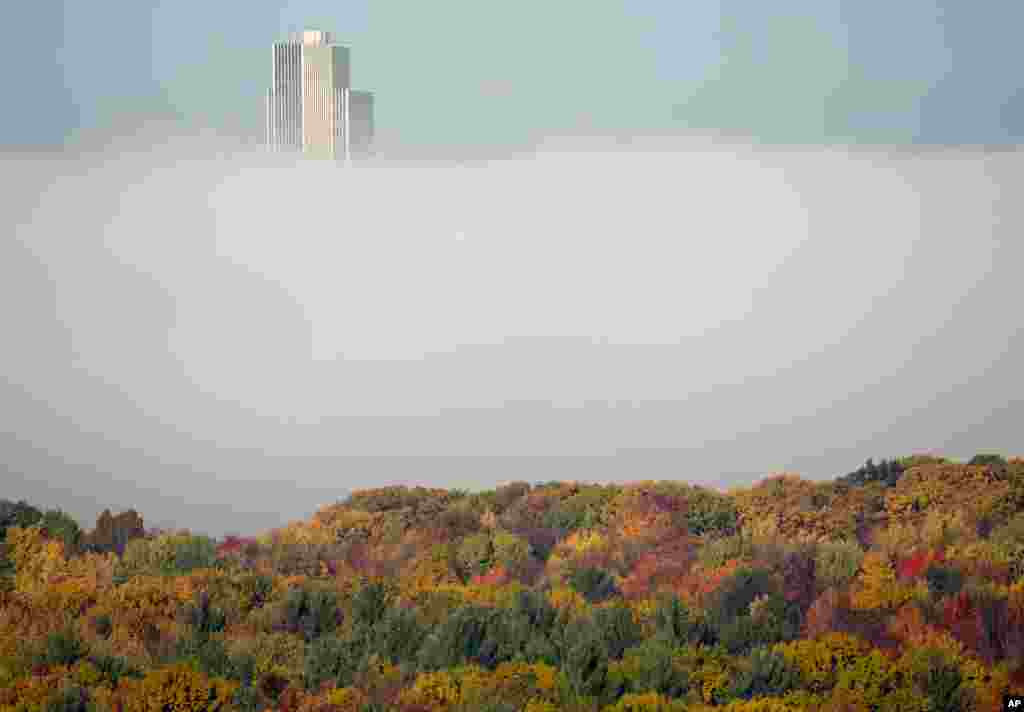 The Corning Tower at the Empire State Plaza in Albany is shrouded in fall colors and morning fog from the Hudson River as seen from East Greenbush, New York, USA.